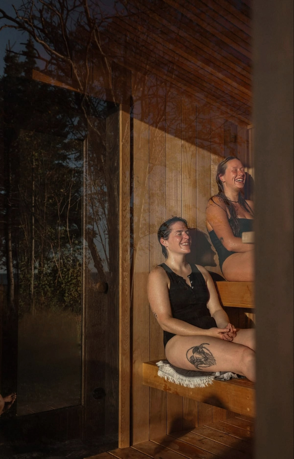 Two people smiling and resting on towels on timber sauna benches