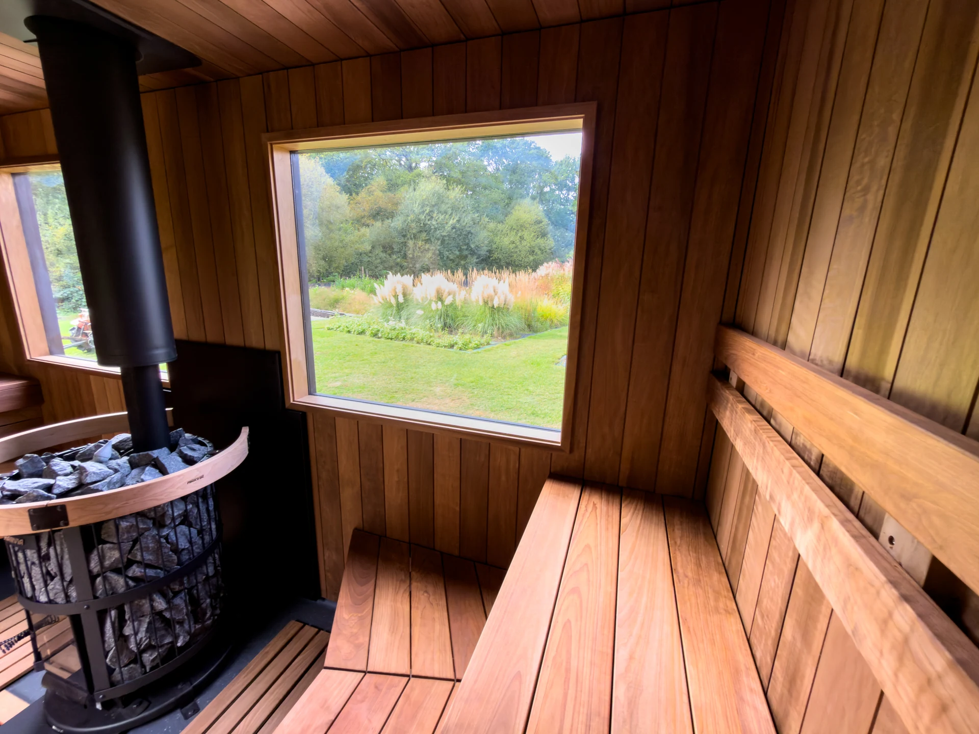 Inside the sauna: a stone-filled black stove, a window onto the garden and stepped timber benches